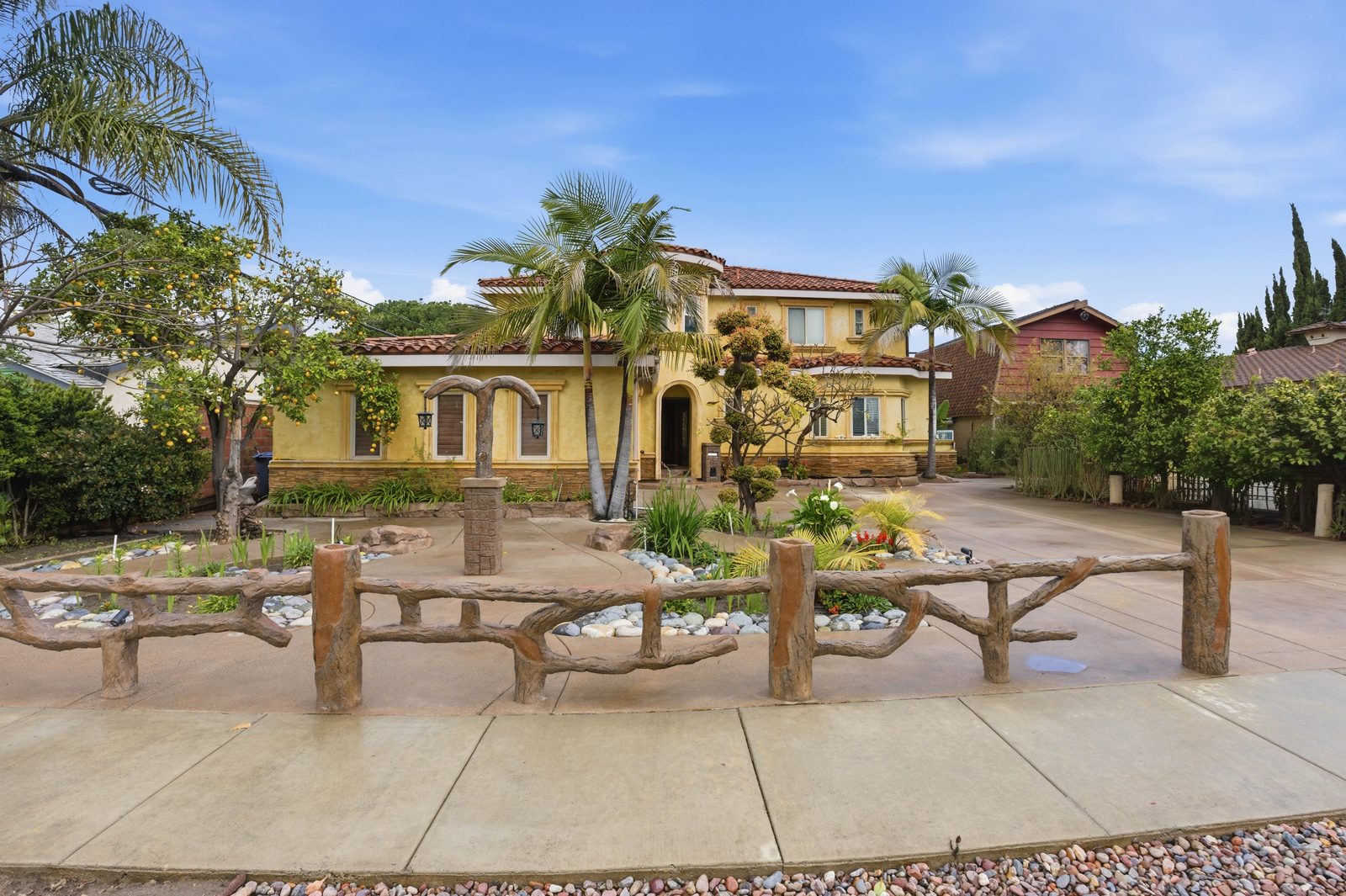 A two story Spanish style house with palms and a log fence
