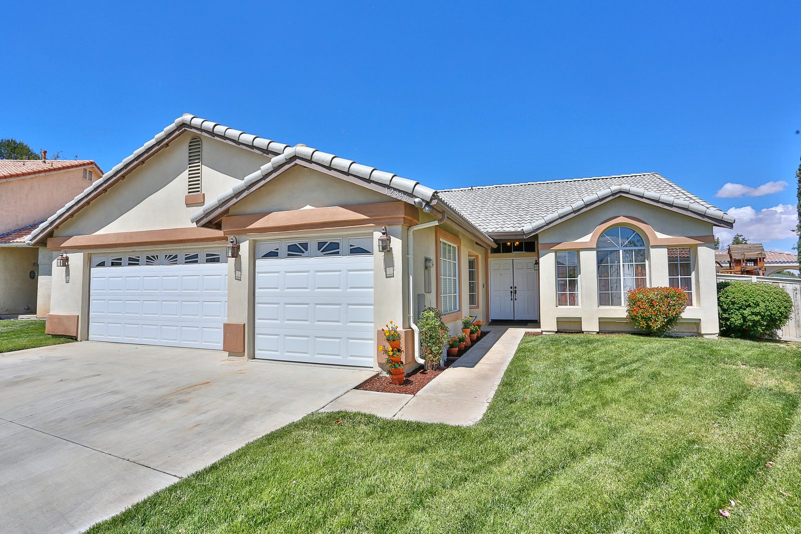 A tan stucco ranch house with a green lawn and two garages